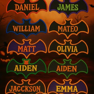 May include: A collection of embroidered bat-shaped patches with names like Daniel, James, and Olivia. Each patch features a different color combination for the bat outline and name lettering. The background is a Halloween-themed scene with bats and an orange sky.
