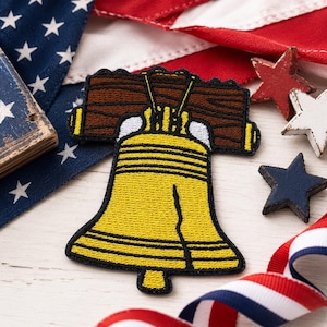 May include: An embroidered patch featuring the Liberty Bell in yellow thread with a brown wooden yoke and a prominent black crack line running down the center. The patch is outlined in black thread and displays a detailed stitched texture.