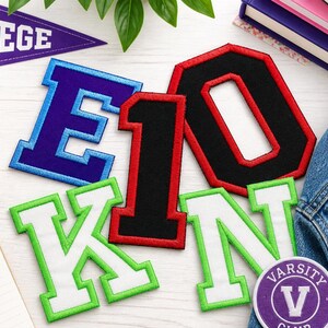 May include: A collection of embroidered varsity letters and a patch, including the letters E, K, N, and the number 10. The letters are in various colors, such as blue, green, and red, with white accents. A purple pennant reads "COLLEGE".