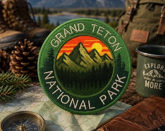 May include: A circular embroidered patch featuring a green border with the text GRAND TETON NATIONAL PARK. The centre depicts a mountain range in shades of green under a bright yellow sun and orange sky, with a dark green forest in the foreground.