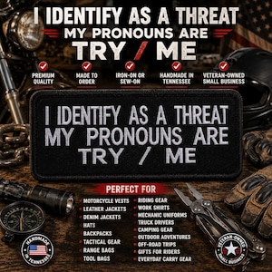 May include: A rectangular black embroidered patch featuring white text that reads I IDENTIFY AS A THREAT MY PRONOUNS ARE TRY / ME. The patch has a thick black border and is designed for attachment to clothing or gear with a clean, bold font style.