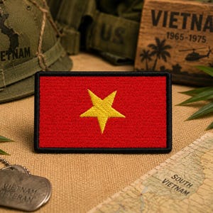 May include: A rectangular embroidered patch featuring a solid red background with a centered, five-pointed yellow star. The patch has a thick, black stitched border surrounding the entire perimeter, creating a distinct frame for the flag design.