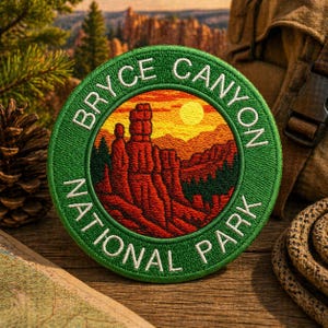 Pode incluir: Um patch redondo bordado com o texto "BRYCE CANYON NATIONAL PARK" em branco sobre uma borda verde. O centro apresenta uma paisagem com formações rochosas vermelhas, um pôr do sol e árvores. O patch está em uma superfície de madeira.