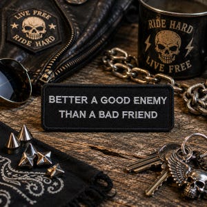 May include: A rectangular black embroidered patch featuring the white text "BETTER A GOOD ENEMY THAN A BAD FRIEND" in a clean, sans-serif font. The patch has a stitched border and is positioned horizontally, showcasing a clear, high-contrast design.