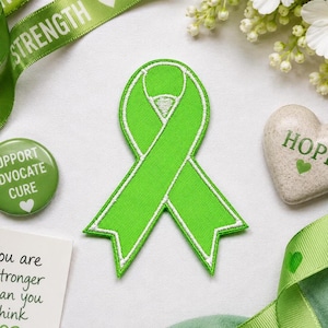 May include: A bright lime green awareness ribbon patch featuring a white embroidered border. The ribbon is shaped with a loop at the top and two pointed tails at the bottom, showcasing a clean, stitched fabric texture throughout the design.