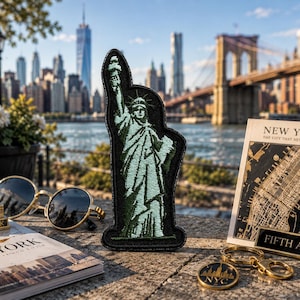May include: A collection of New York City souvenirs, including a Statue of Liberty patch, a miniature Empire State Building, sunglasses, a map, and a keychain. The background features the NYC skyline, the Brooklyn Bridge, and the East River.