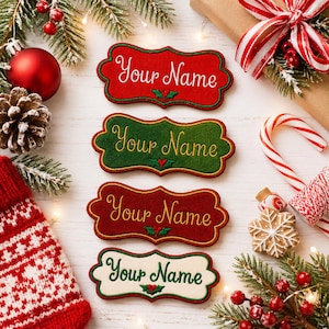 May include: Four scalloped-edge fabric name tags with embroidered text reading Your Name. The tags are red, green, dark red, and cream, each featuring a small holly leaf accent. They are arranged vertically on a white surface with holiday decor.