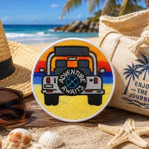 May include: A circular embroidered patch featuring a rear view of a grey off-road vehicle against a sunset background of orange, red, blue, and yellow stripes. The spare tyre cover displays the text ADVENTURE AWAITS with a central compass icon.
