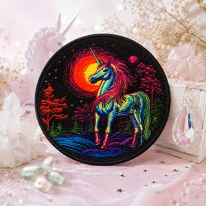 May include: A circular embroidered patch featuring a vibrant unicorn with a rainbow-colored mane and body standing in a dark forest landscape. A large, glowing orange sun sits in the background, with small stars and trees surrounding the unicorn.