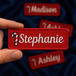 May include: Red rectangular name patches with white embroidered names and a candy cane graphic. The name "Stephanie" is prominently displayed on the front patch, with other names like "Madison" and "Ashley" visible in the background. The patches are on a dark blue fabric.
