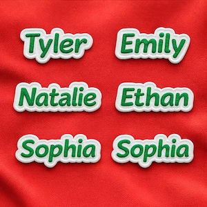May include: Embroidered name patches in green lettering with a white border, displayed on a red fabric background. Names include Tyler, Emily, Natalie, Ethan, and Sophia. These patches are ideal for personalizing clothing or accessories.