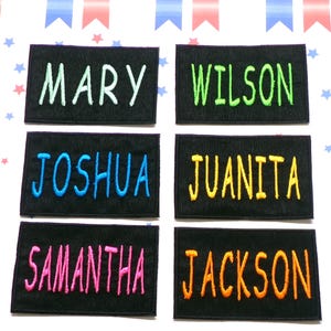 Puede incluir: Seis parches de tela negra con diferentes nombres bordados en hilo de colores. Los nombres son Mary, Wilson, Joshua, Juanita, Samantha y Jackson.