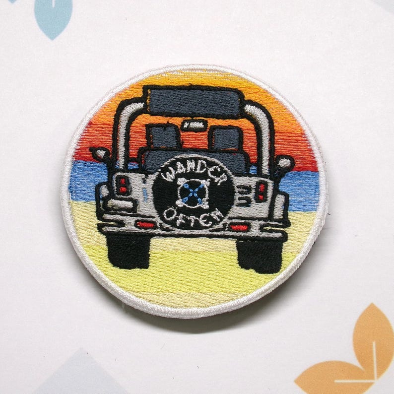 May include: A round embroidered patch featuring a white jeep with a black spare tire that says "Wander Often" in a circle. The jeep is driving on a beach with a sunset in the background.