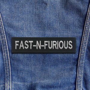 Puede incluir: Un parche rectangular negro con el texto bordado "FAST-N-FURIOUS" en blanco. El parche está sobre un fondo de mezclilla azul, probablemente una chaqueta o chaleco.