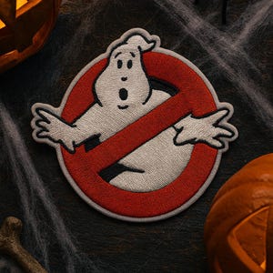 May include: Embroidered patch featuring the Ghostbusters logo, a white ghost inside a red circle with a red slash. The patch is surrounded by Halloween decorations, including carved pumpkins, a spider, and a bone.