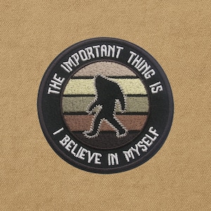 Op de afbeelding: Ronde geborduurde patch met een zwart silhouet van Bigfoot tegen een zonsondergangontwerp. De tekst "The Important Thing Is I Believe In Myself" is in het wit. De patch heeft een zwarte rand en is geplaatst tegen een bruinachtige achtergrond.