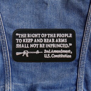 May include: A black patch with white text and a rifle graphic, sewn onto a denim jacket. The patch reads "THE RIGHT OF THE PEOPLE TO KEEP AND BEAR ARMS SHALL NOT BE INFRINGED." with "2nd Amendment, U.S. Constitution" below.