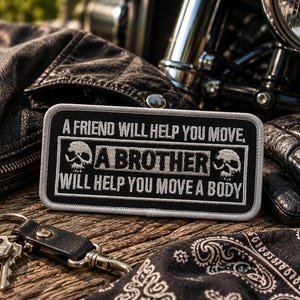 Puede incluir: Parche bordado en blanco y negro con el texto "A FRIEND WILL HELP YOU MOVE, A BROTHER WILL HELP YOU MOVE A BODY" y gráficos de calaveras. El parche está sobre una superficie de madera con una chaqueta de cuero, una motocicleta, guantes, llaves y una bandana.