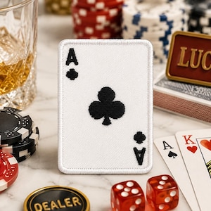 May include: A white Ace of Clubs patch with black details stands upright among poker chips, dice, and playing cards. A glass of amber liquid and a "LUCKY" sign are also visible, creating a casino theme.
