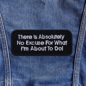 Pode incluir: Um patch bordado preto com o texto branco: "There Is Absolutely No Excuse For What I'm About To Do". O patch retangular com cantos arredondados está sobre um fundo de ganga.