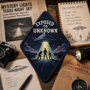 May include: A diamond-shaped embroidered patch featuring a dark blue night sky with a silver UFO emitting a bright yellow beam of light over three human silhouettes. The text EXPOSED TO UNKNOWN is stitched in white at the top of the patch.