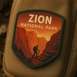 Puede incluir: Parche con el texto "ZION NATIONAL PARK" y una ilustración de un excursionista en un cañón. El parche tiene un borde verde y está sobre un fondo de tela beige.