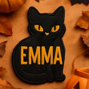 May include: Black cat patch with the name "EMMA" in yellow lettering. The cat has yellow eyes and is surrounded by Halloween decorations, including pumpkins, leaves, and a bat.