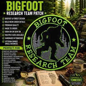 May include: A circular embroidered patch featuring a black silhouette of Bigfoot against a grey forest background, surrounded by a neon green border with the text BIGFOOT RESEARCH TEAM and two stars in neon green thread on a black fabric base.