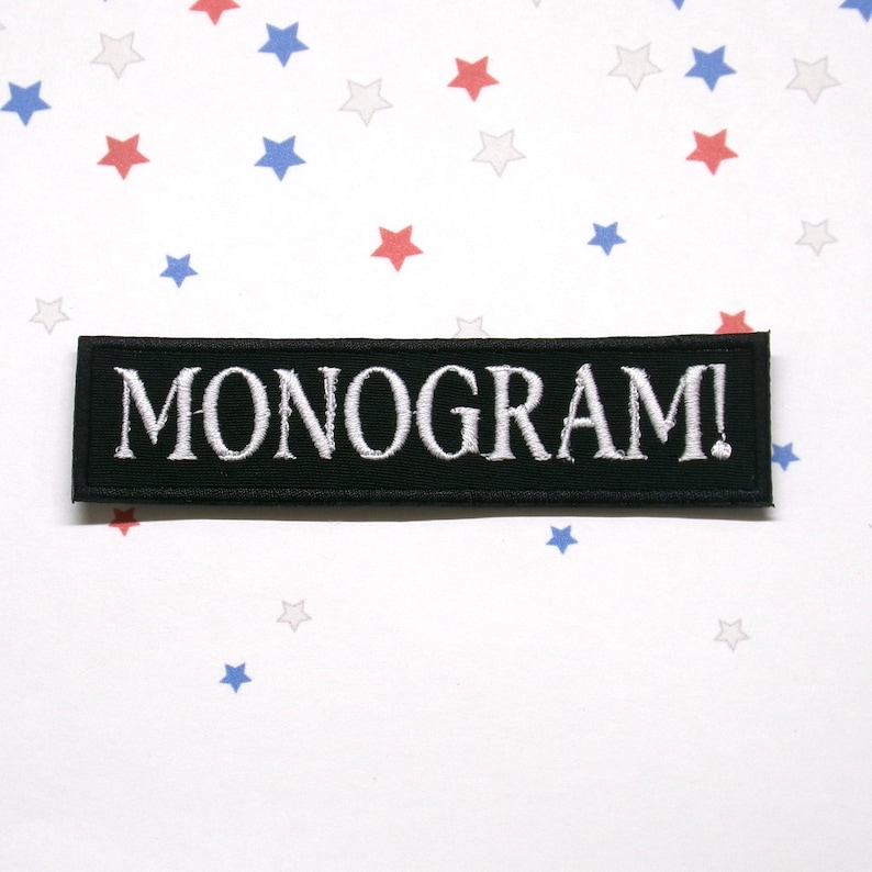 Pu&ograve; includere: Una toppa rettangolare nera con la scritta "MONOGRAM!" ricamata in bianco. La toppa &egrave; posta su uno sfondo bianco cosparso di stelle rosse, bianche e blu.