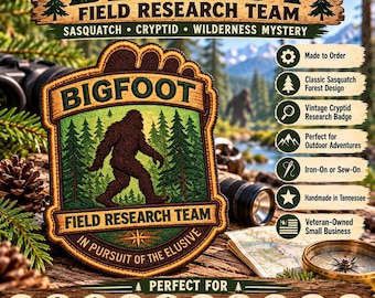 May include: A brown and green embroidered patch shaped like a footprint, featuring a silhouette of Bigfoot in a forest. The text reads BIGFOOT FIELD RESEARCH TEAM and IN PURSUIT OF THE ELUSIVE. The patch has a dark brown border.