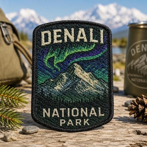 May include: A rectangular embroidered patch featuring a mountain peak under a vibrant green and purple aurora borealis. The text DENALI is stitched in white at the top, and NATIONAL PARK is stitched in white at the bottom, all on a black background.