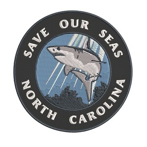 May include: Embroidered patch with a shark leaping out of the water. The patch is round with the text "SAVE OUR SEAS NORTH CAROLINA" in white on a black background. The shark is white and gray.