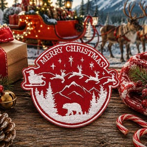 May include: A circular red embroidered patch featuring white stitching of a bear in a forest, mountains, and a sleigh pulled by reindeer. The text MERRY CHRISTMAS is arched across the top. The design includes stars and a snowy landscape scene.