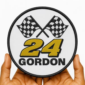 Puede incluir: Parche bordado circular con el número 24 dorado y el nombre "GORDON" debajo. Dos banderas a cuadros en blanco y negro cruzadas en la parte superior. El parche tiene un borde negro y un fondo blanco.
