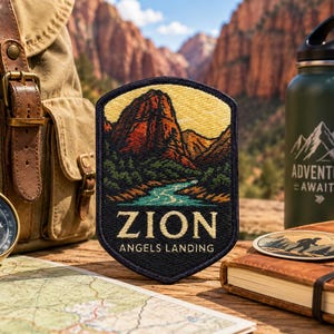 Peut inclure: Un écusson brodé en forme de bouclier représentant un paysage du parc national de Zion avec une rivière, des montagnes et le texte ZION ANGELS LANDING en lettres blanches. L'écusson a une bordure sombre et est présenté parmi du matériel.