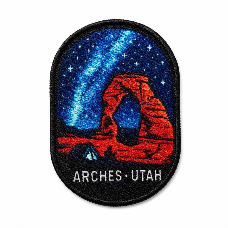 Op de afbeelding: Een ovaal geborduurde patch met een rode rotsboogformatie onder een donkerblauwe nachtelijke hemel vol met een heldere sterrenstelsel. Een kleine blauwe tent is zichtbaar aan de voet van de boog. De tekst ARCHES UTAH staat onderaan in het wit.