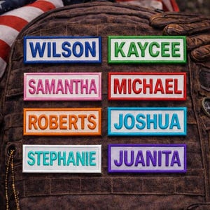 May include: Rectangular embroidered patches with names in white lettering. Names include WILSON, KAYCEE, SAMANTHA, MICHAEL, ROBERTS, JOSHUA, STEPHANIE, and JUANITA. Each patch has a colored border: blue, green, pink, red, orange, light blue, white, and purple. Patches are affixed to a brown backpack.