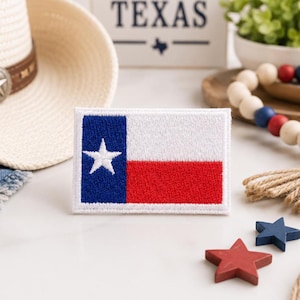 May include: A rectangular embroidered patch featuring the Texas state flag design. The patch displays a vertical blue stripe on the left with a single white star, followed by horizontal white and red stripes on the right, all bordered in white.