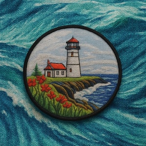 May include: Embroidered patch featuring a lighthouse on a rocky coast with red flowers in the foreground. The lighthouse has a white tower and a red roof. The patch is round with a black border and set against a blue wave pattern.