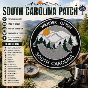May include: A circular embroidered patch featuring a white bear silhouette filled with green pine trees and a yellow sun. The black border contains the white text WANDER OFTEN and SOUTH CAROLINA. The patch is displayed with a compass and binoculars.