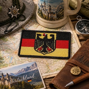 May include: A rectangular embroidered patch featuring the German flag with horizontal black, red, and gold stripes. Centered on the flag is a black eagle emblem with red beak and claws, rendered in detailed thread work with a black stitched border.