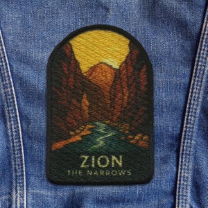 Op de afbeelding: Een rechthoekige patch met een landschapsscène van Zion National Park. Het ontwerp omvat een rivier, canyonwanden en een zonsondergang. De tekst "ZION THE NARROWS" wordt in gouden letters weergegeven.
