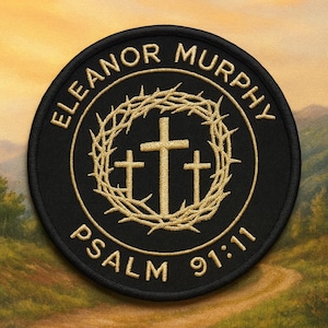 Puede incluir: Parche redondo bordado en negro con texto y diseño dorado. El texto dice "ELEANOR MURPHY" en la parte superior, "PSALM 91:11" en la parte inferior. Una corona de espinas dorada rodea tres cruces.