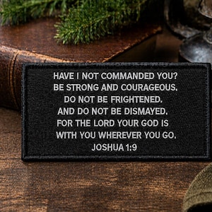 May include: A black rectangular patch with white embroidered text. The text reads: "HAVE I NOT COMMANDED YOU? BE STRONG AND COURAGEOUS. DO NOT BE FRIGHTENED. AND DO NOT BE DISMAYED. FOR THE LORD YOUR GOD IS WITH YOU WHEREVER YOU GO. JOSHUA 1:9."