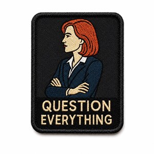 May include: A rectangular embroidered patch with a black background featuring a profile illustration of a person with shoulder-length red hair wearing a dark blue blazer over a white shirt with arms crossed. The text QUESTION EVERYTHING is in beige.