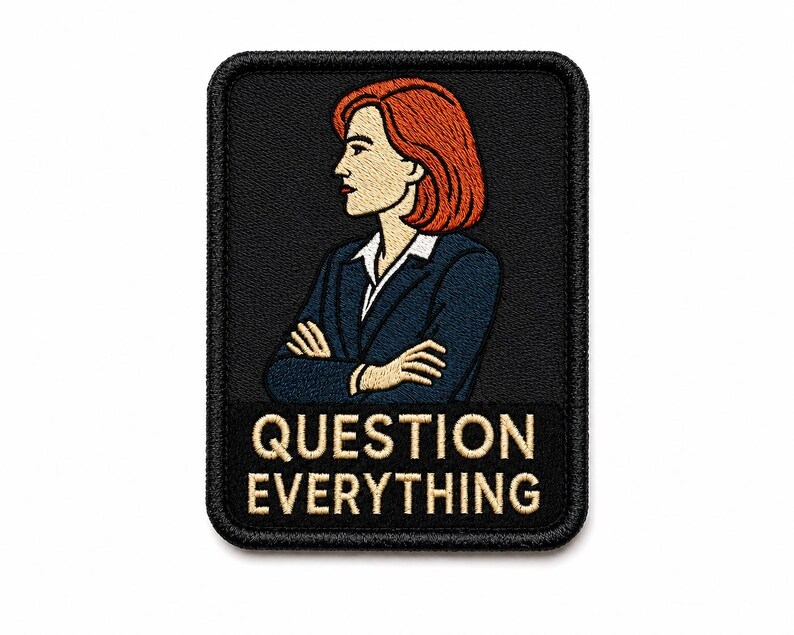 May include: A rectangular embroidered patch with a black background featuring a profile illustration of a person with shoulder-length red hair wearing a dark blue blazer over a white shirt with arms crossed. The text QUESTION EVERYTHING is in beige.