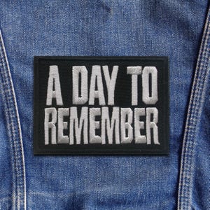 May include: A rectangular black patch with the embroidered text "A DAY TO REMEMBER" in white. The patch is sewn onto a blue denim jacket.