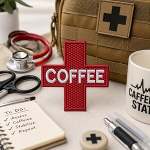 May include: A red cross-shaped patch with the word "COFFEE" in white, alongside medical tools and a mug with a caffeine-related design. A notepad lists "To Do" items: Assess, Caffeine, Stabilize, and Repeat. A tan medical bag is in the background.