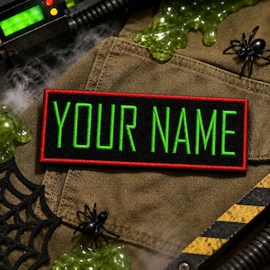 May include: A rectangular embroidered patch with a black background and a bright red border. The text "YOUR NAME" is stitched in a vibrant neon green font across the center of the patch, featuring a clean, sans-serif, block-style typeface.