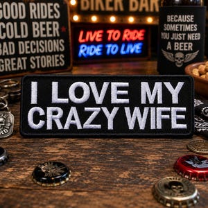 May include: A rectangular black embroidered patch with white stitched text that reads I LOVE MY CRAZY WIFE. The patch features a clean, bold font and a finished border, designed for attachment to clothing or accessories with a clear, legible message.